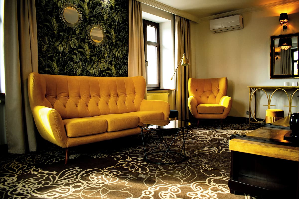 A room with a yellow sofa, a matching armchair, a small table, and a decorative mirror.