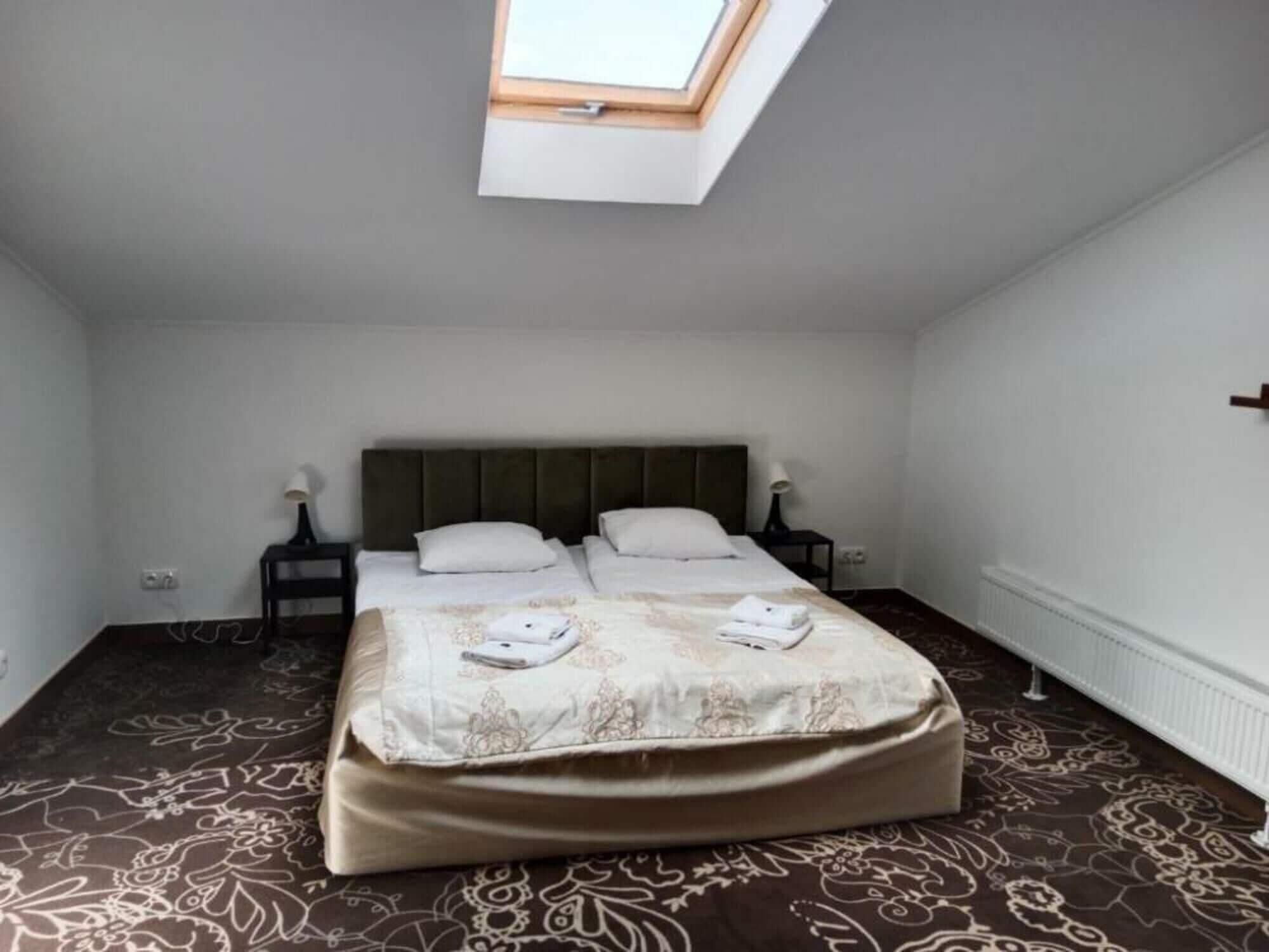 A bedroom with a skylight, a bed with a patterned bedspread, two bedside tables with lamps, and a radiator on the wall.