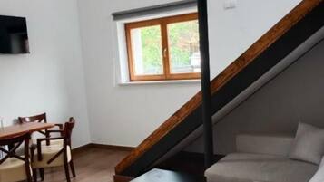 Una sala de estar moderna con una escalera de madera, un comedor con mesa y sillas, y un amplio ventanal que proporciona luz natural.