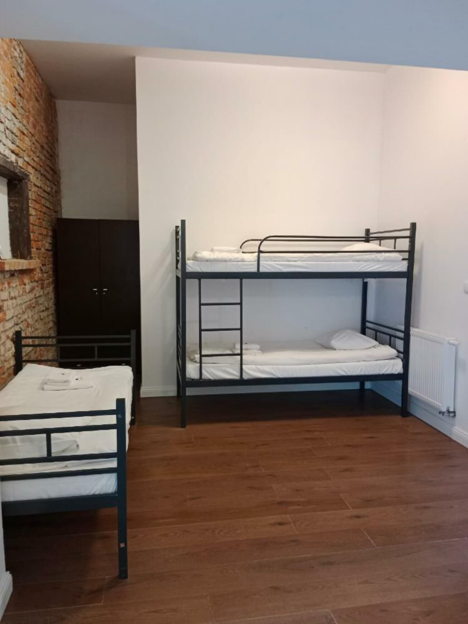 A room with two bunk beds, a wooden floor, a brick wall, and a black wardrobe.