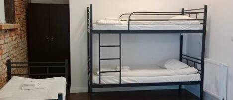 A room with two bunk beds, a wooden floor, a brick wall, and a black wardrobe.