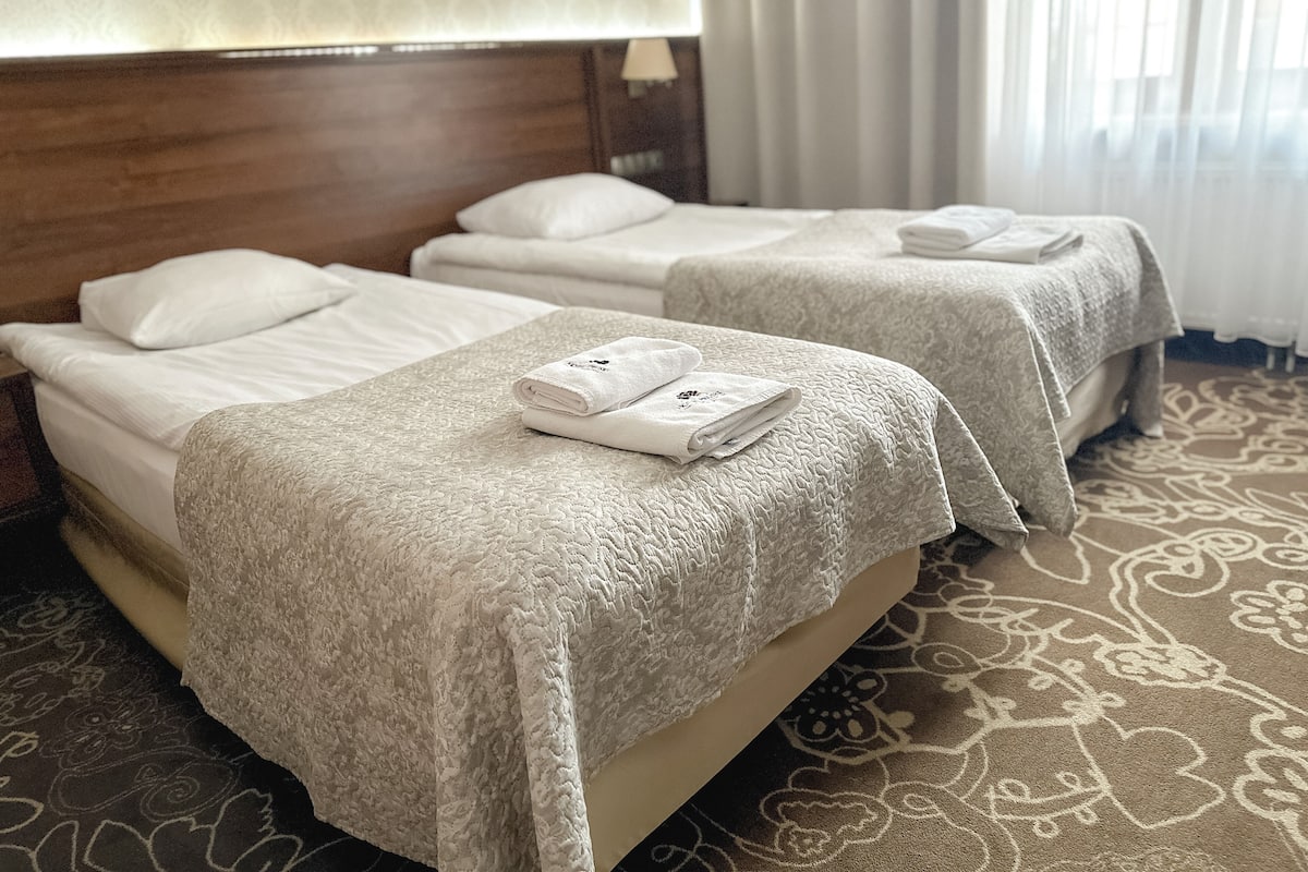 Two single beds with white linens and a textured blanket, a wooden headboard, and a patterned carpet.