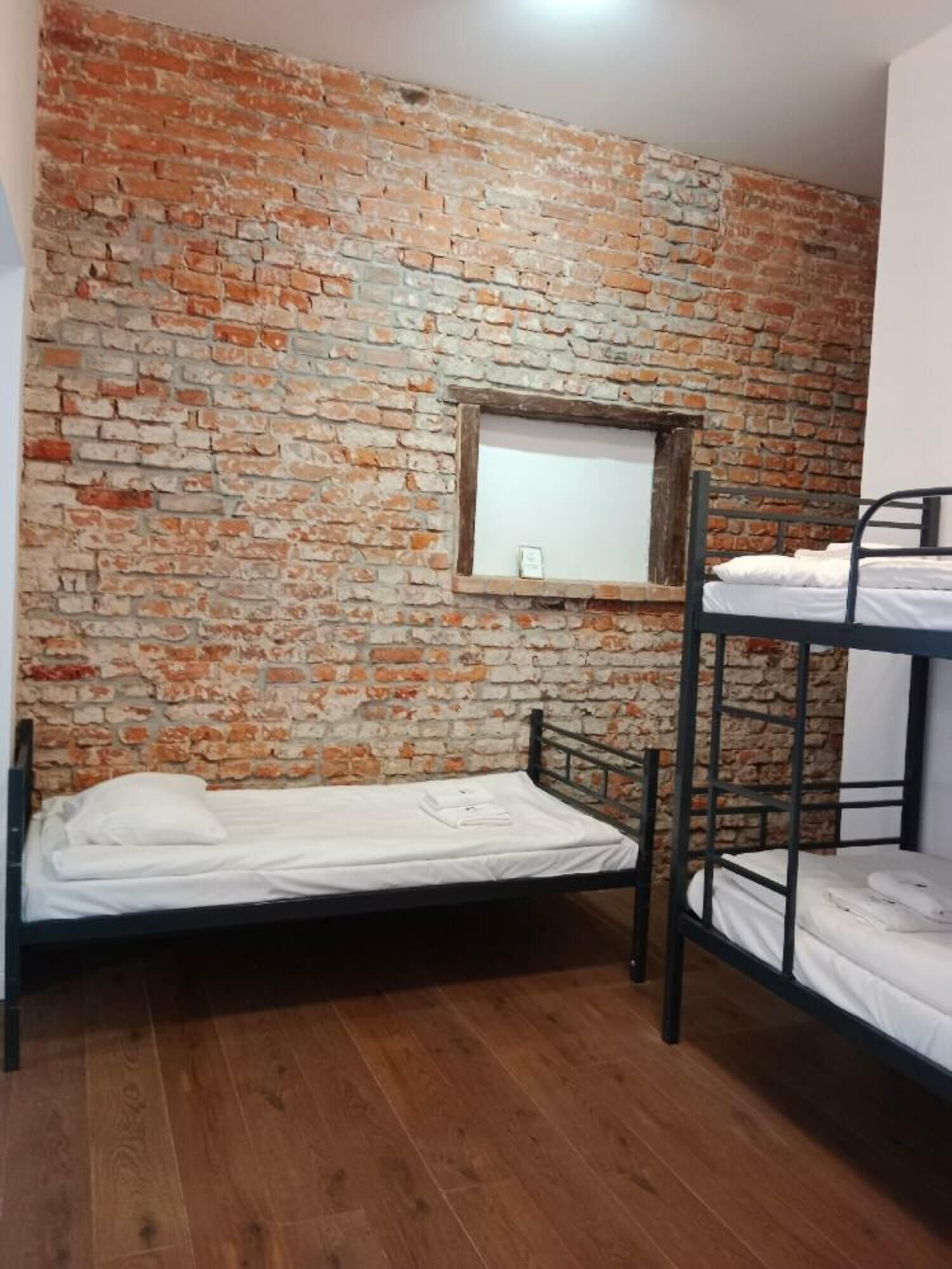 Une chambre de dortoir avec un mur en briques, un lit superposé et un lit simple.