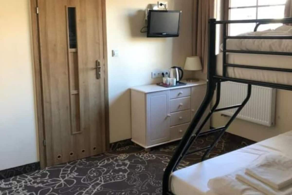 A hotel room with a bunk bed, a wooden door, a small desk with a television, and a patterned carpet.