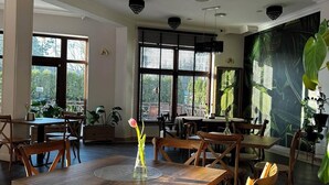 A spacious dining area with wooden tables and chairs, large windows with blinds, and decorative lighting fixtures.