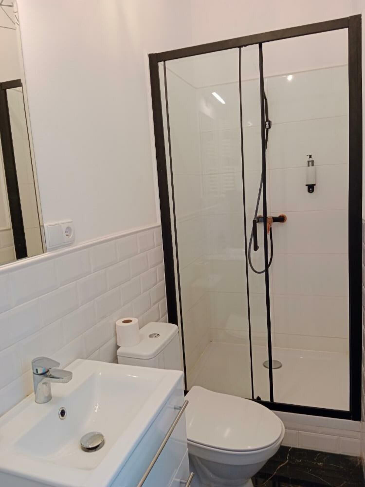 Een badkamer met een douche met glazen wand, een witte wastafel en een toilet.