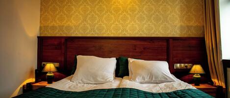 Habitación de hotel con cabecera de madera, colcha verde, dos almohadas blancas y dos lámparas de noche.