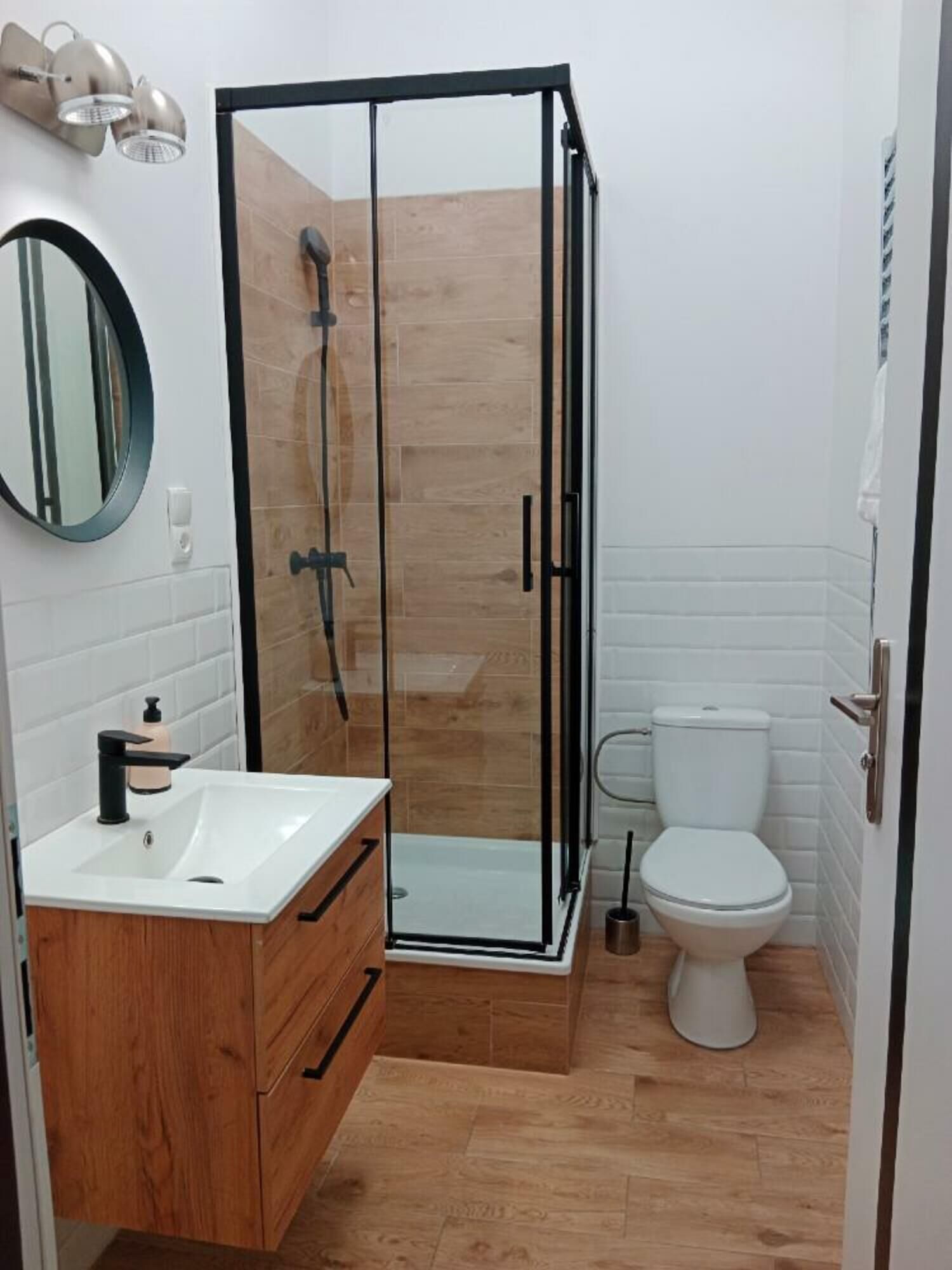 Un bany modern amb dutxa tancada amb vidre, un lavabo blanc amb armari de fusta i un vàter.