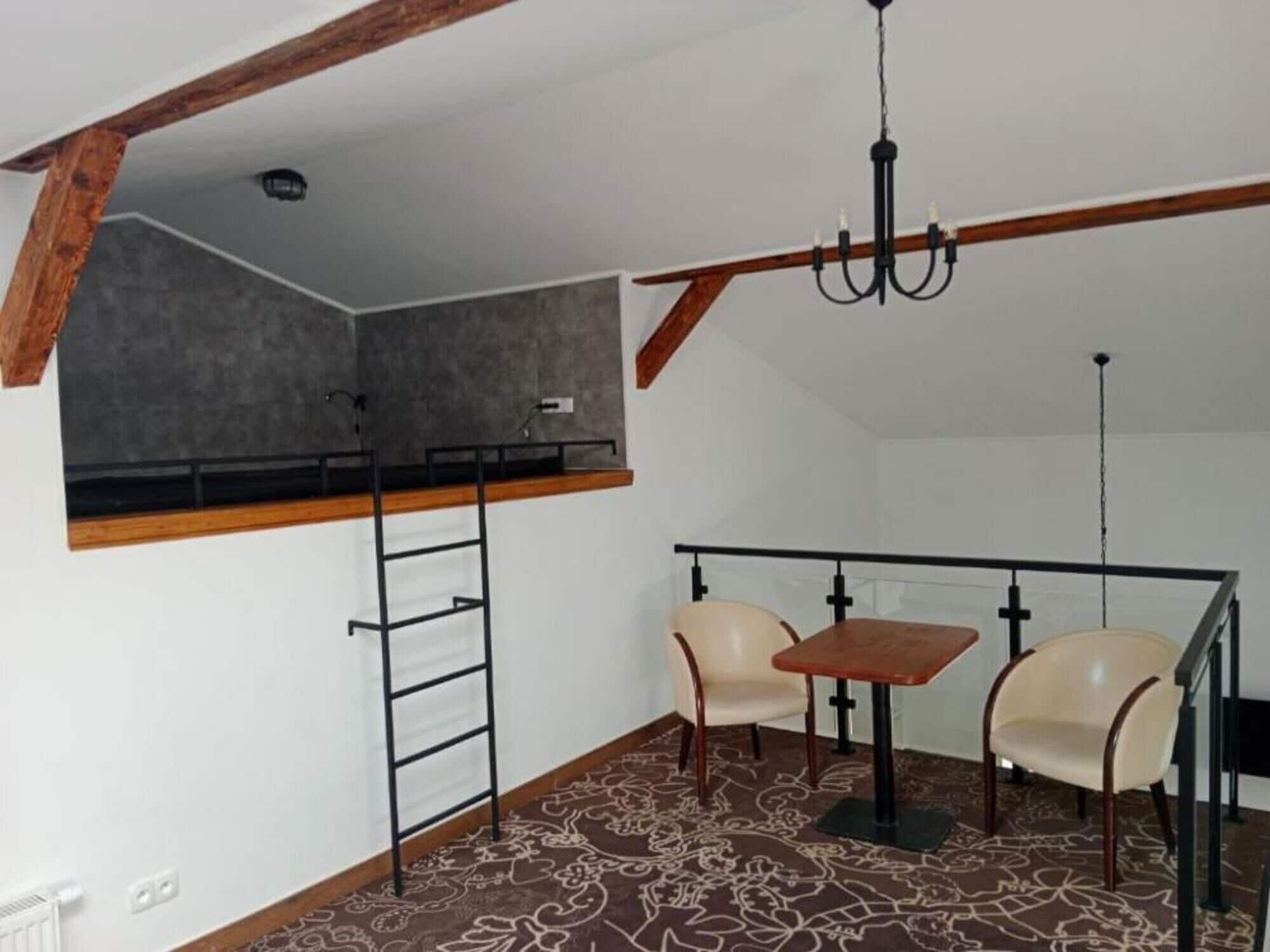 Ett rum med en säng på ett loft, ett skrivbord, två stolar och en kristallkrona.