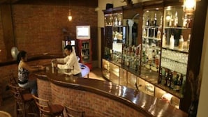 Un espace bar avec un comptoir en briques, des tabourets de bar et un présentoir à bouteilles avec des miroirs.