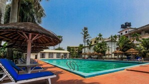 Un espace piscine avec des chaises longues, un parasol en chaume et des palmiers.
