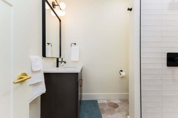 Un baño con lavamanos, espejo, toallero y dispensador de papel higiénico.