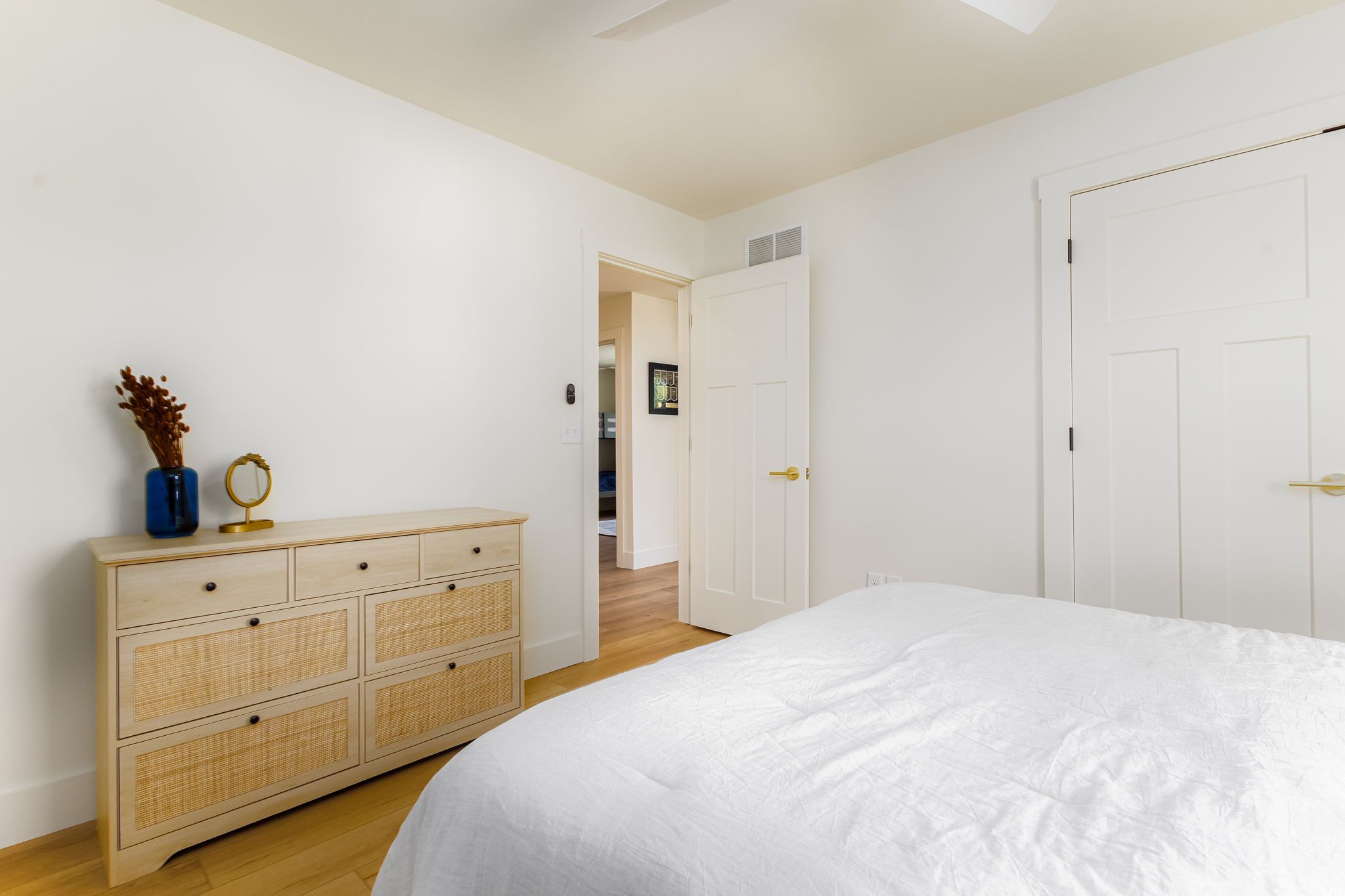 Een slaapkamer met een groot bed, een houten dressoir en witte wanden.