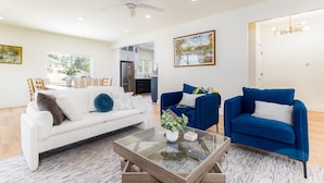 A modern living room with a white sofa, a blue armchair, and a glass coffee table.