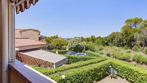 Une vue depuis un balcon donnant sur un jardin aménagé, avec des haies soigneusement taillées et quelques voitures garées au loin.