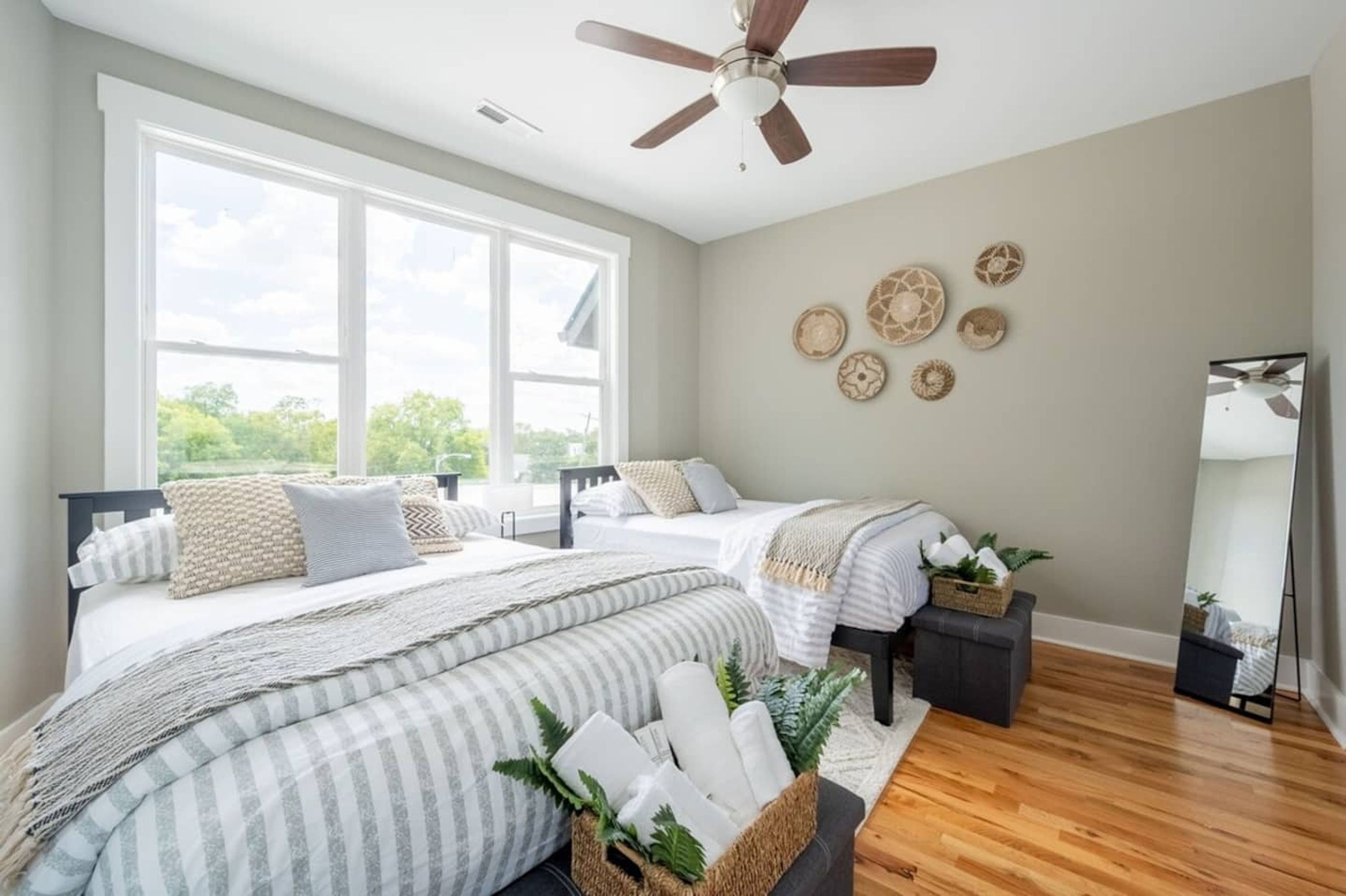 Une chambre avec deux lits, un ventilateur de plafond, de grandes fenêtres et des éléments de décoration murale.