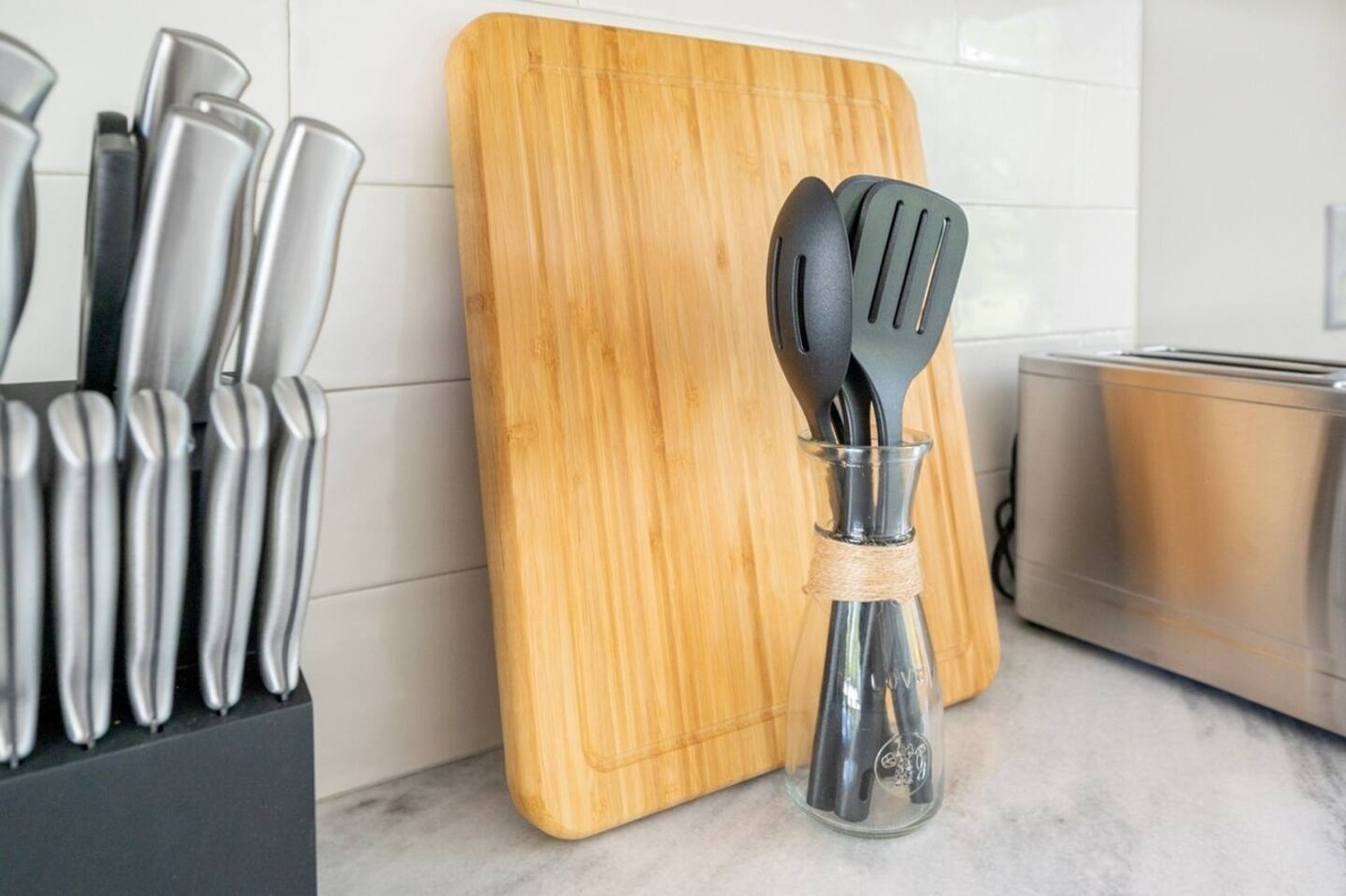 A kitchen counter with a wooden cutting board, a knife block, and a glass jar holding kitchen utensils.