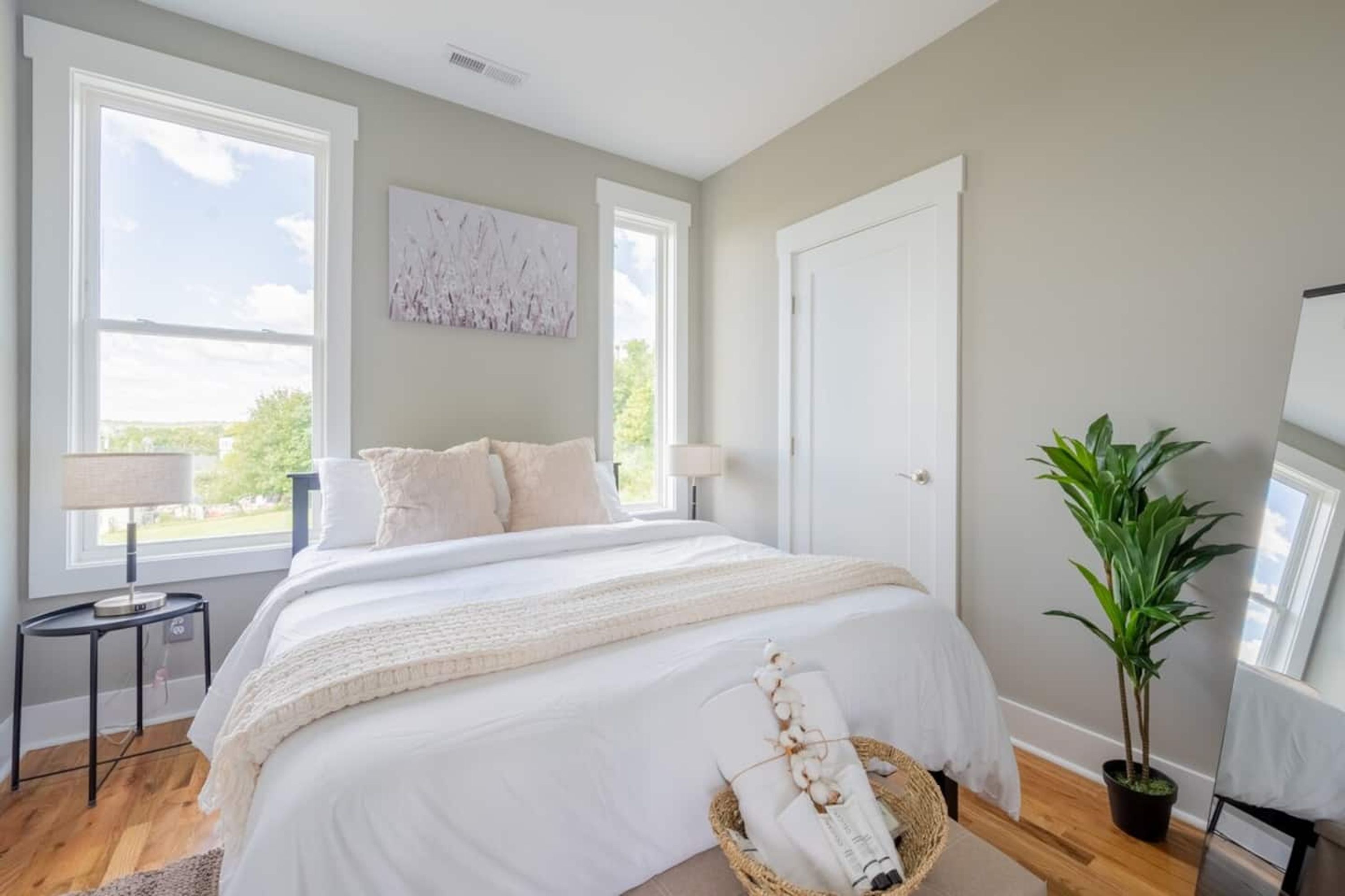 A bedroom with a large bed, two bedside tables, a potted plant, and a window with a view.