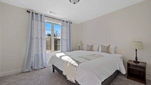 Ein Schlafzimmer mit einem großen Bett, zwei Nachttischlampen, einem Fenster mit Vorhängen und einer Deckenleuchte.