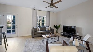 Un salon moderne avec un canapé gris, une table basse, un téléviseur et un ventilateur de plafond.