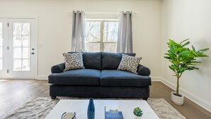 A living room with a dark blue sofa, patterned pillows, a white coffee table with a book, a vase, and a potted plant. - 1 King 2 Queens Garage Yard Washer Dryer (Old Hickory)