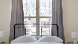 A bed with a metal frame, white bedding, and a view of buildings through a window with grey curtains. - 1 King 2 Queens Garage Yard Washer Dryer (Old Hickory)