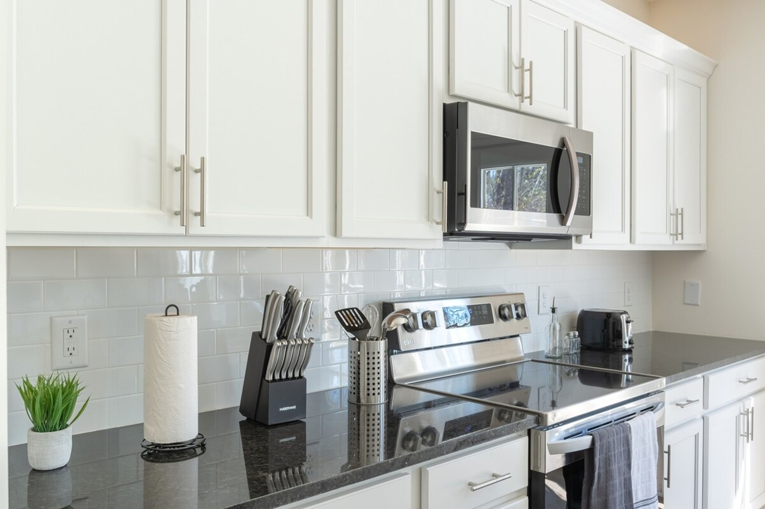A modern kitchen with white cabinets, a stainless steel oven, a microwave, and a granite countertop.