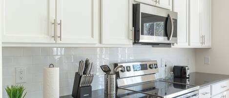 A modern kitchen with white cabinets, a stainless steel oven, a microwave, and a granite countertop.
