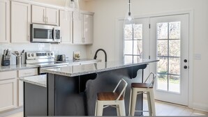 Una cocina moderna con gabinetes blancos, un microondas de acero inoxidable, horno empotrado, encimera de granito y una isla grande con taburetes de bar.