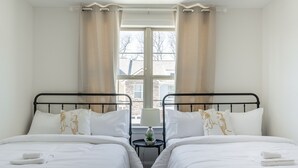 Una habitación doble con dos camas, una mesita con lámpara y una ventana con cortinas.