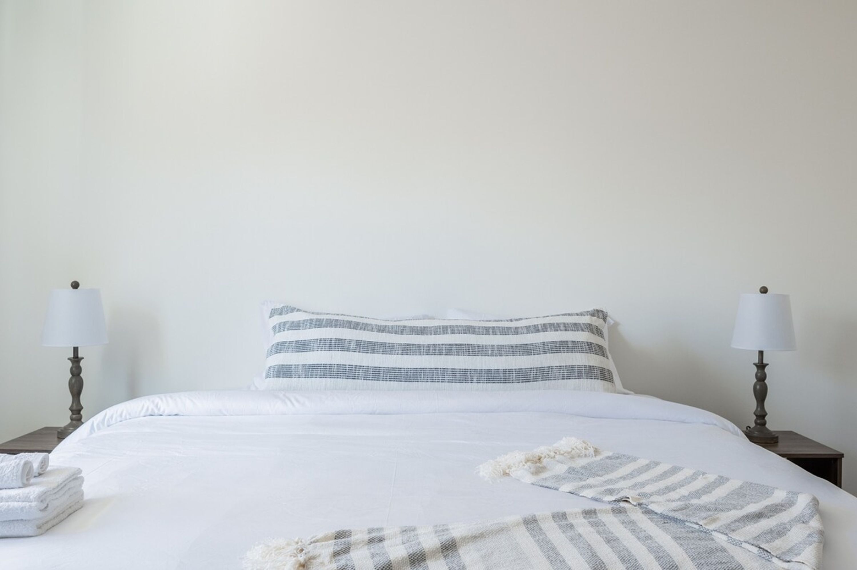 A neatly made bed with striped bedding, two bedside lamps, and folded towels on a nightstand.