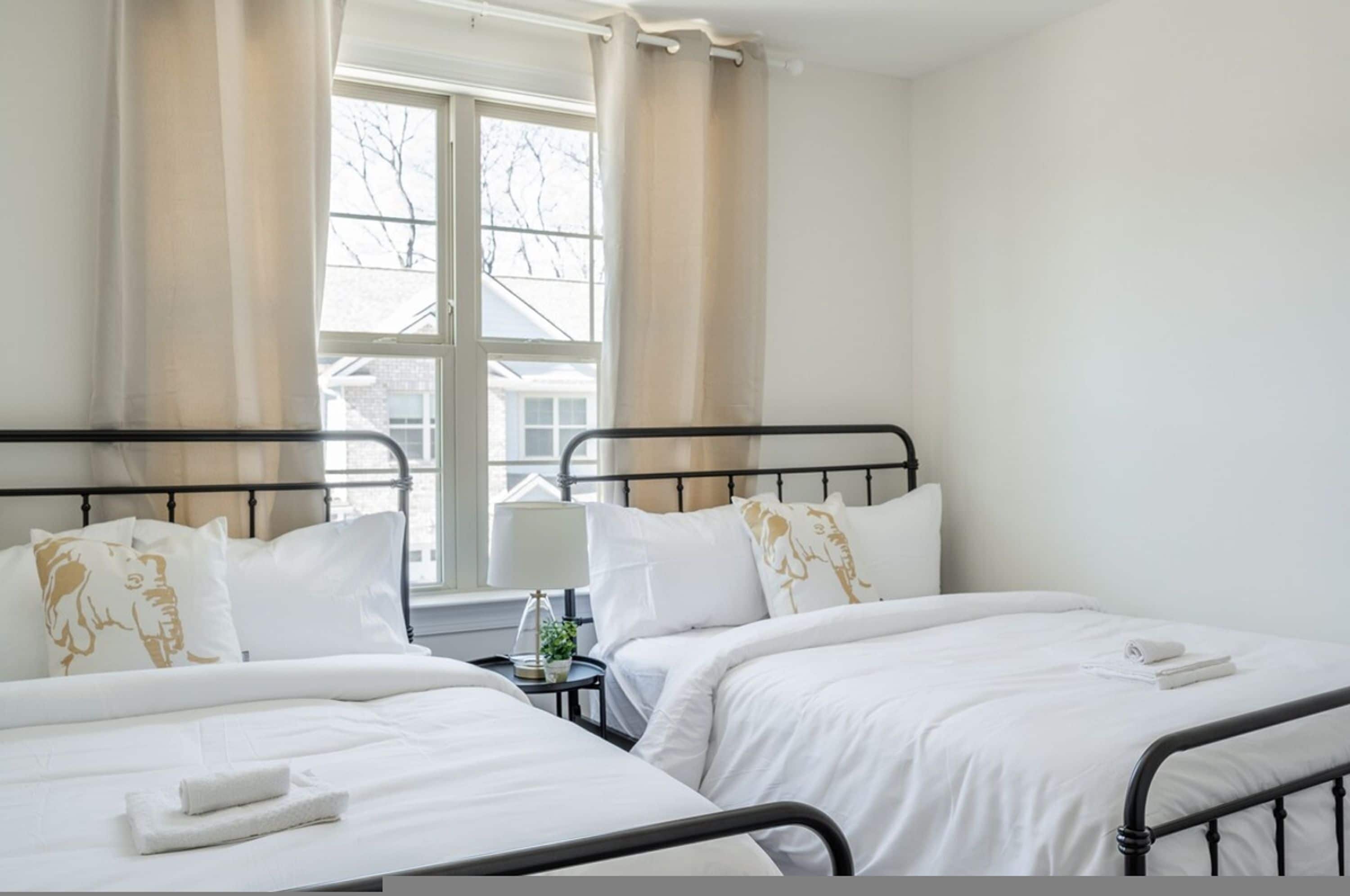 Hotelkamer met twee bedden, een raam met gordijnen, een nachtkastje met een lamp en uitzicht op buiten.
