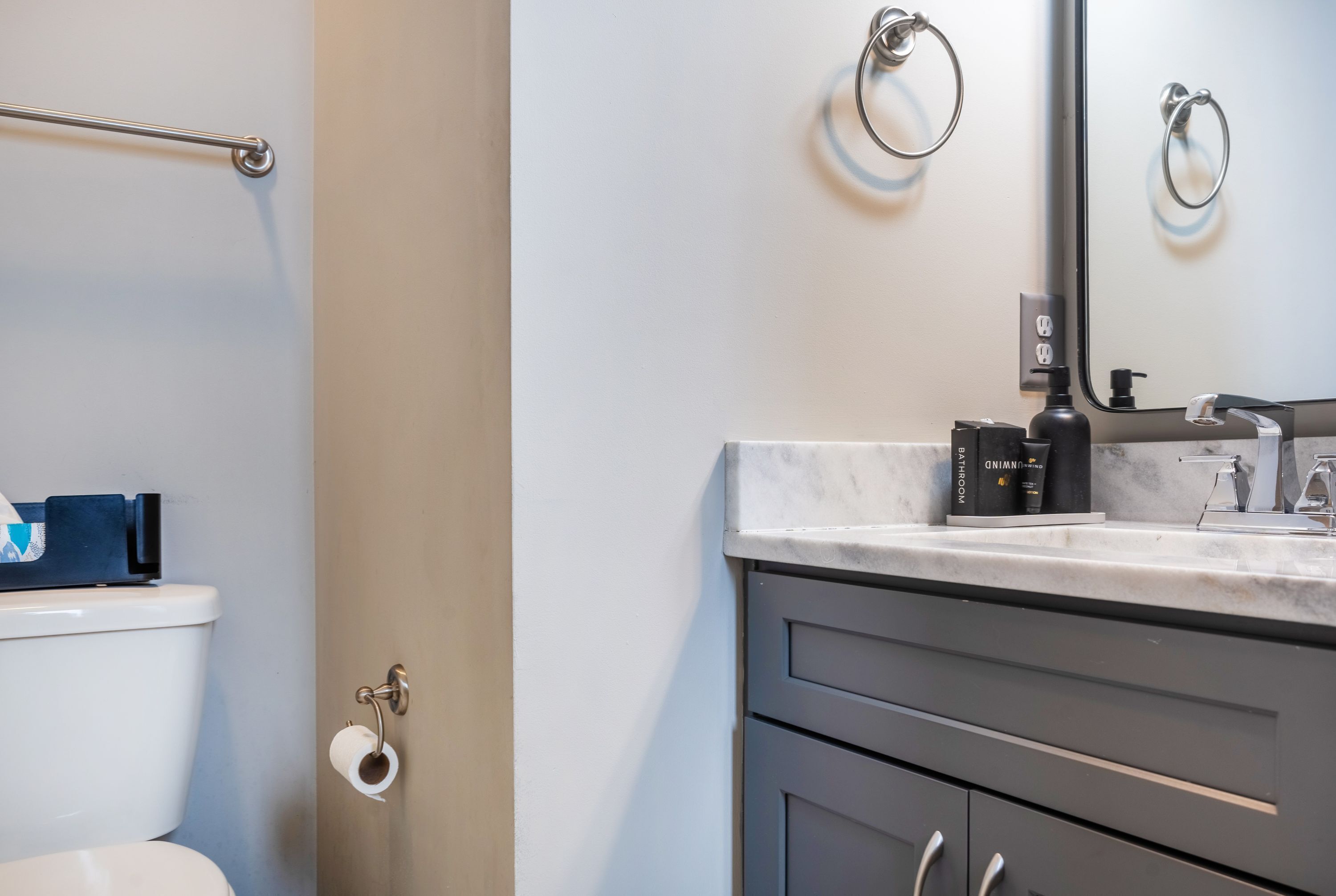 A modern bathroom with a toilet, a towel ring, a mirror, a soap dispenser, and a toilet paper holder.