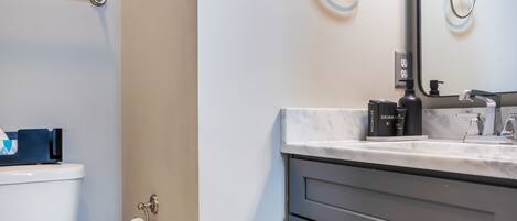 A modern bathroom with a toilet, a towel ring, a mirror, a soap dispenser, and a toilet paper holder.
