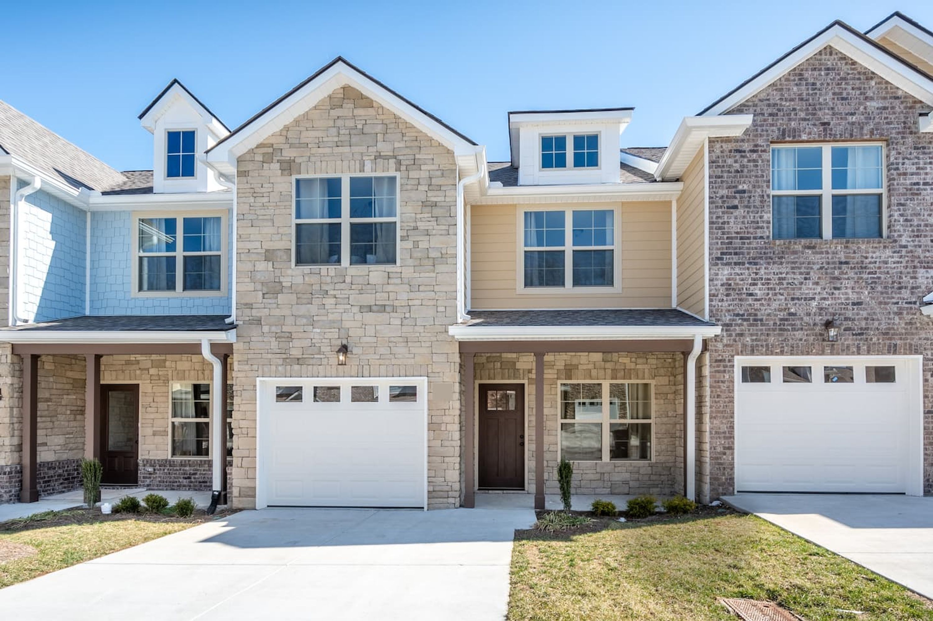 A row of three townhouses with distinct architectural styles, each featuring a garage and a front door.
