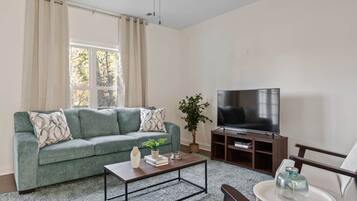 A living room with a green sofa, a coffee table, a TV, and a plant.
