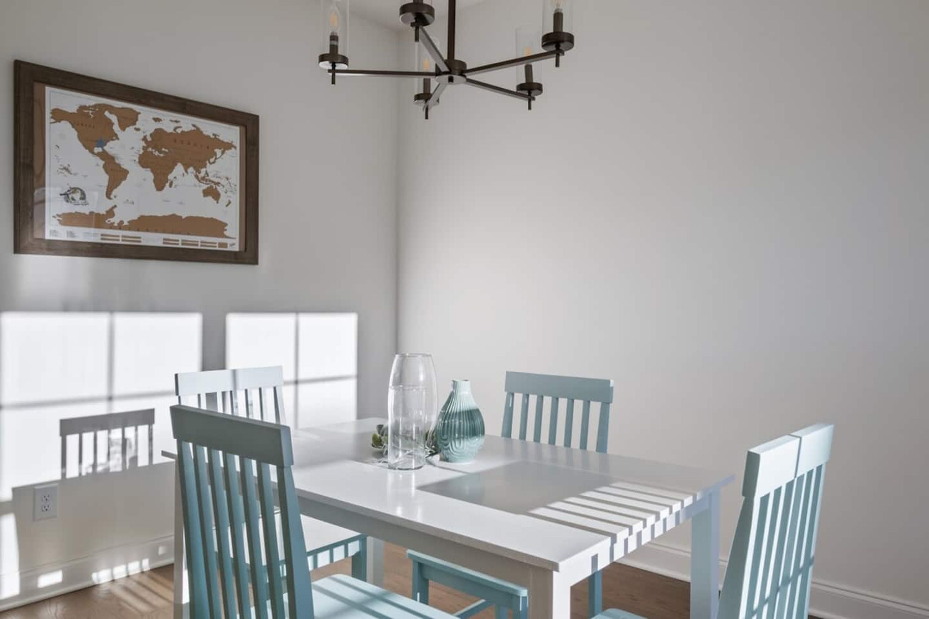 A dining area with a white table, blue chairs, a world map on the wall, and a modern chandelier.
