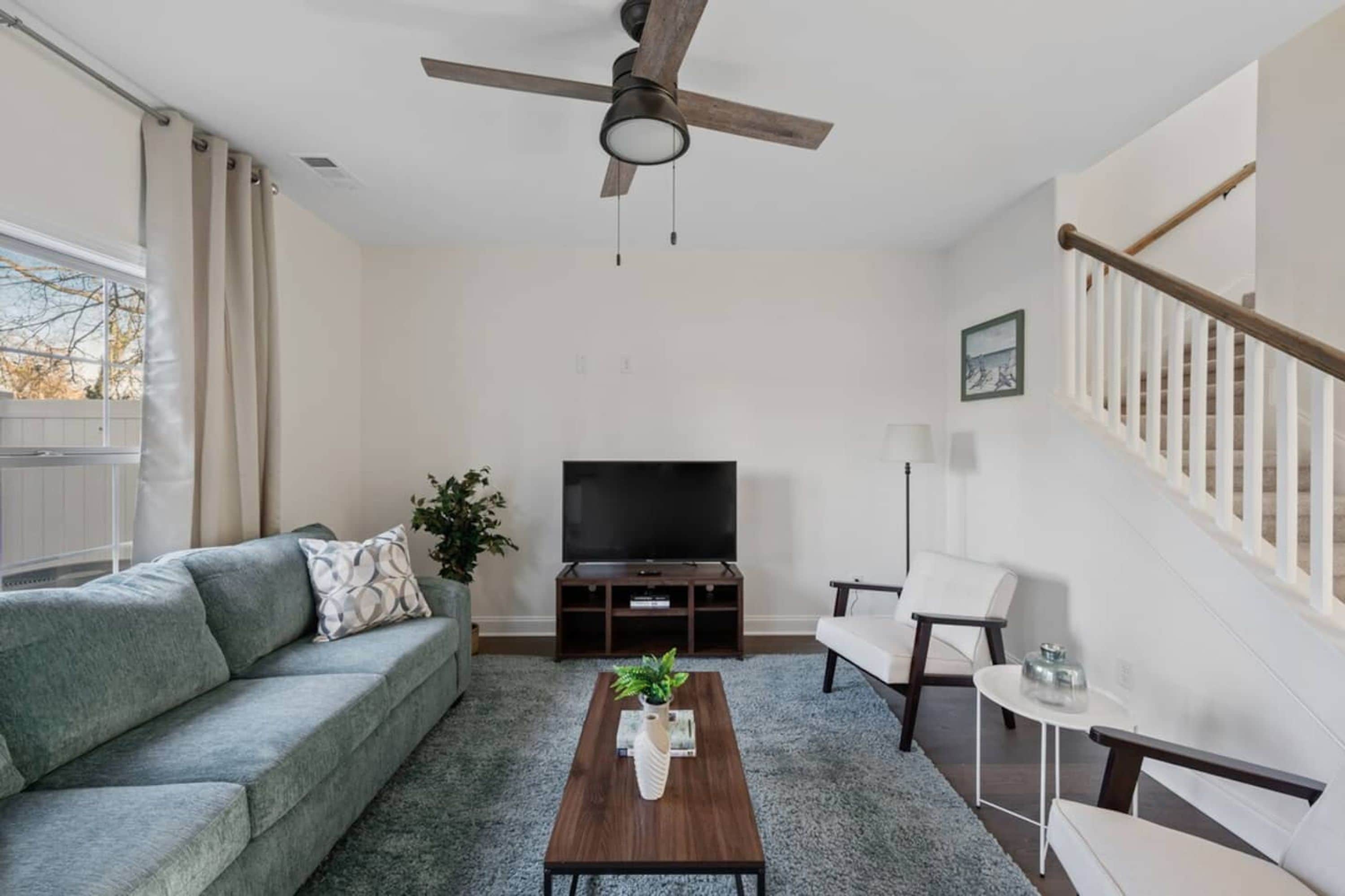 A living room with a sofa, coffee table, TV stand, and a ceiling fan.