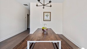 Een eethoek met een houten tafel, een kroonluchter, een ingelijste foto aan de muur en een vaas met bloemen.