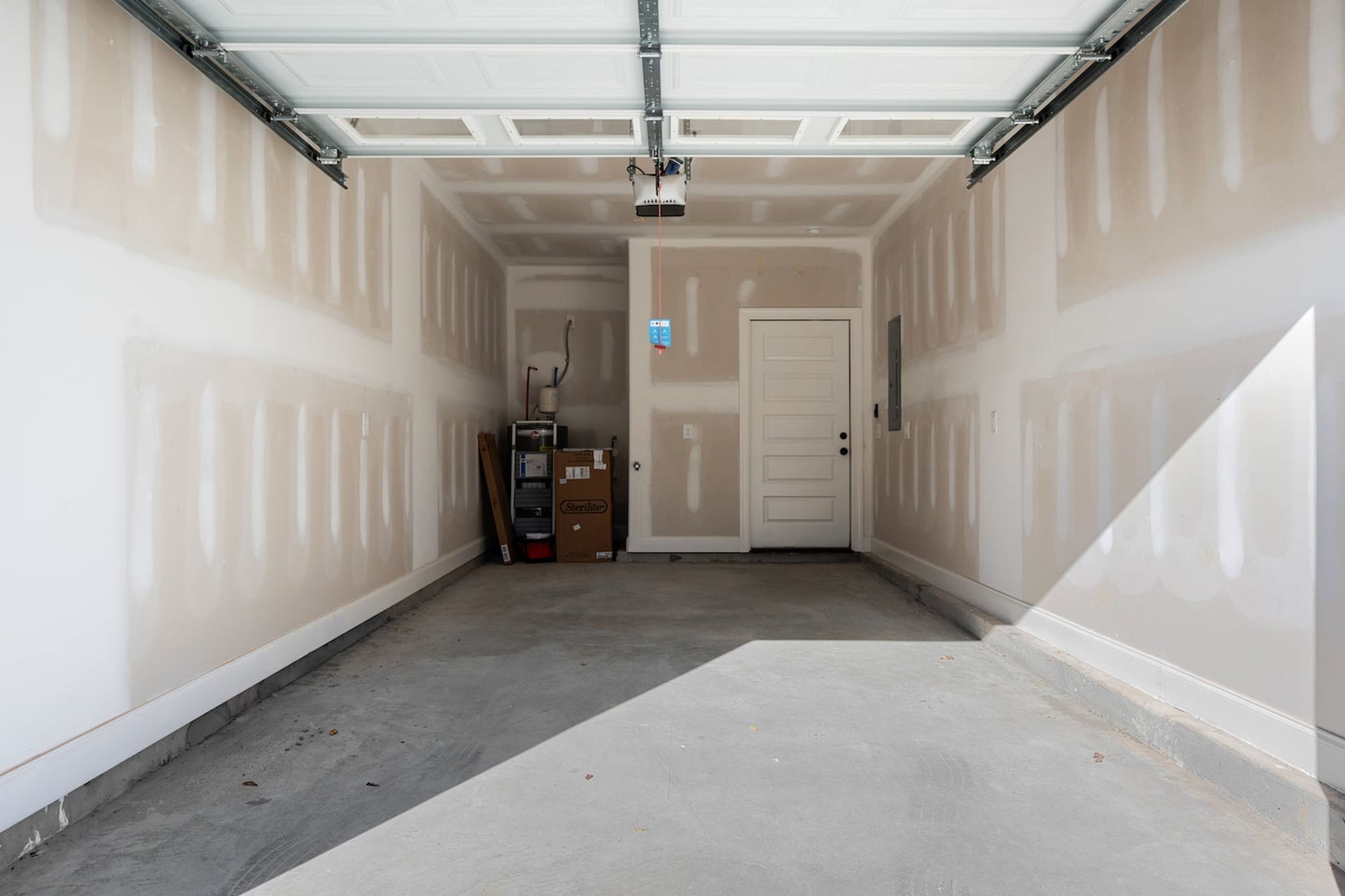 A garage with a white door, a ceiling-mounted projector, and a concrete floor.