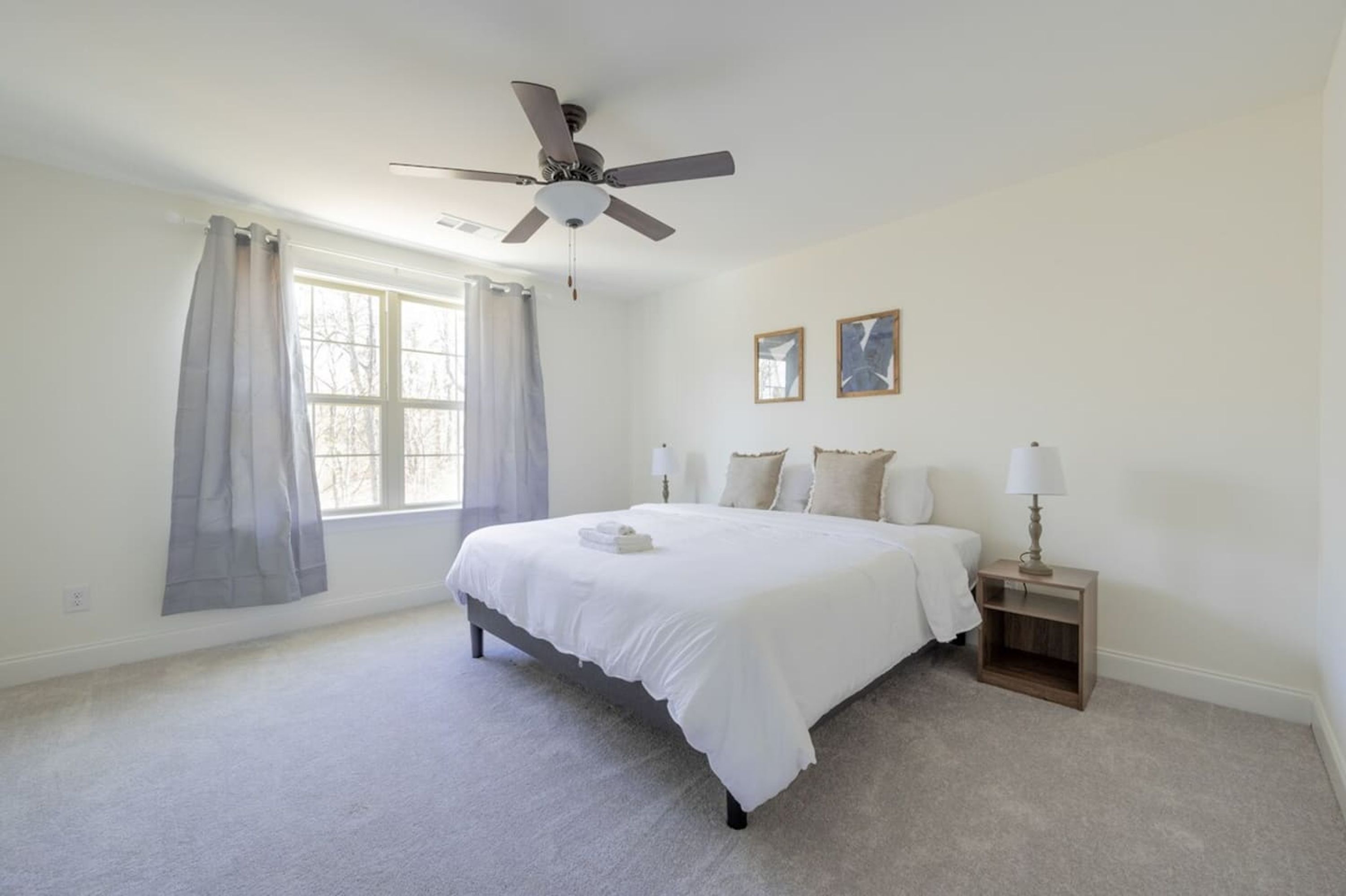 A bedroom with a bed, a ceiling fan, a nightstand, and a window with curtains.