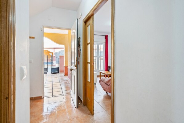 A hallway with a tiled floor leading to a room with a bed and a red curtain. - Apartment in Lepe with Pool and Garden (Lepe)