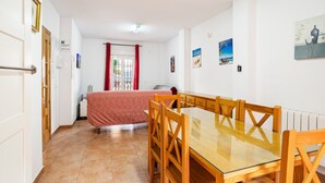 Una habitación con una mesa de comedor de vidrio y sillas de madera, una cama con cubrecama rojo y una ventana con cortinas rojas.
