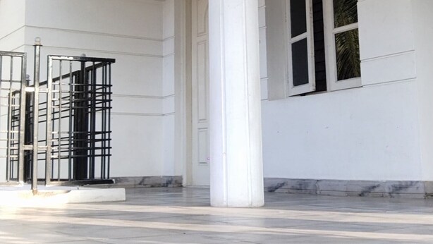 A spacious covered area with a large column, a metal gate, and a window with blinds. - VARSHA ENCLAVE WHITE HOUSE (Mysore)