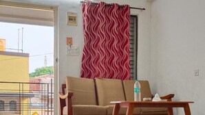 A spacious living area with a ceiling fan, a sofa, a wooden coffee table, and a red patterned curtain. - VARSHA ENCLAVE WHITE HOUSE (Mysore)
