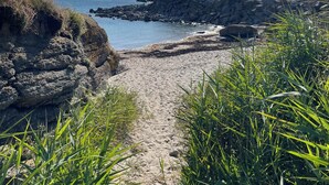 A sandy beach path leading to a rocky shoreline with clear blue water and a bright sun in the sky. - Exceptional villa with ocean views—comfort and charm, Brittany (Lanildut)
