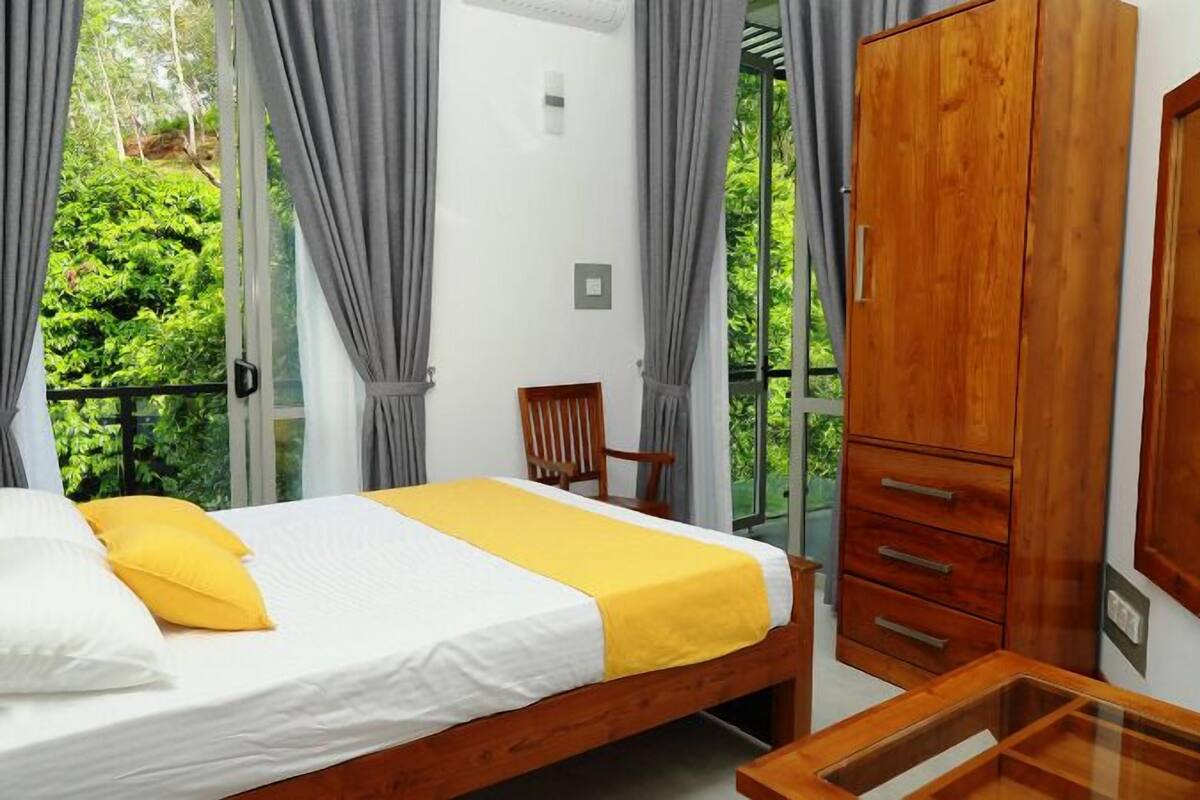 A bedroom with a bed, a wooden wardrobe, a small chair, and a balcony with curtains.