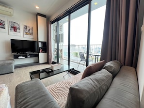 En moderne stue med sofa, fladskærms-TV, sofabord og en balkon med udsigt over byen.
