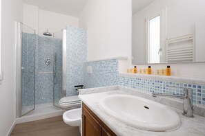 Un baño moderno con ducha de vidrio, lavamanos blanco y retrete.