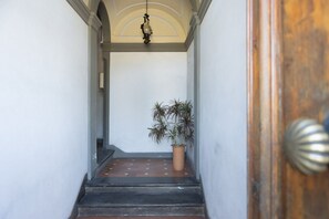 A narrow hallway with a wooden door on the right, a potted plant, and a light fixture above the door. - Serristori Riverside Apartment (Florence)